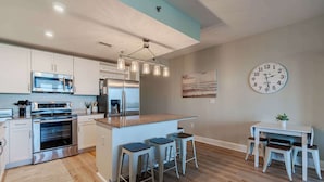 A modern kitchen with stainless steel appliances, a central island with stools, and a dining area with a table and chairs. - Whitesands Retreat Incredible Resort Home! (Panama City Beach)