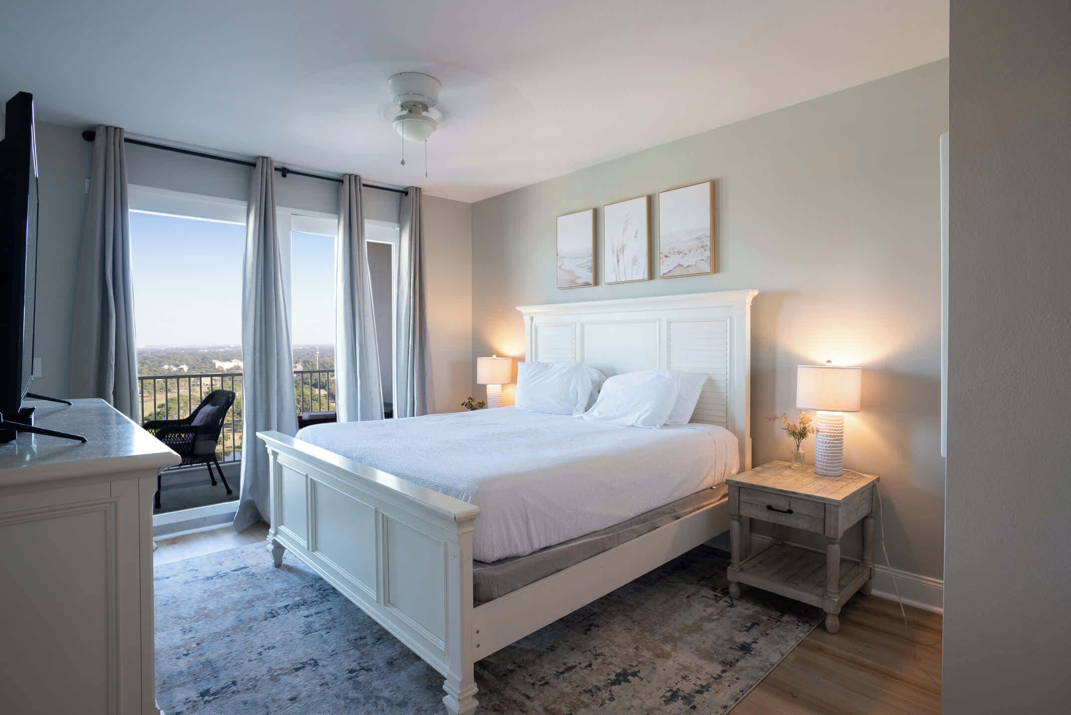 Un dormitorio con una cama grande, una mesita de noche con lámpara, un escritorio con silla y vistas a la ciudad por la ventana.