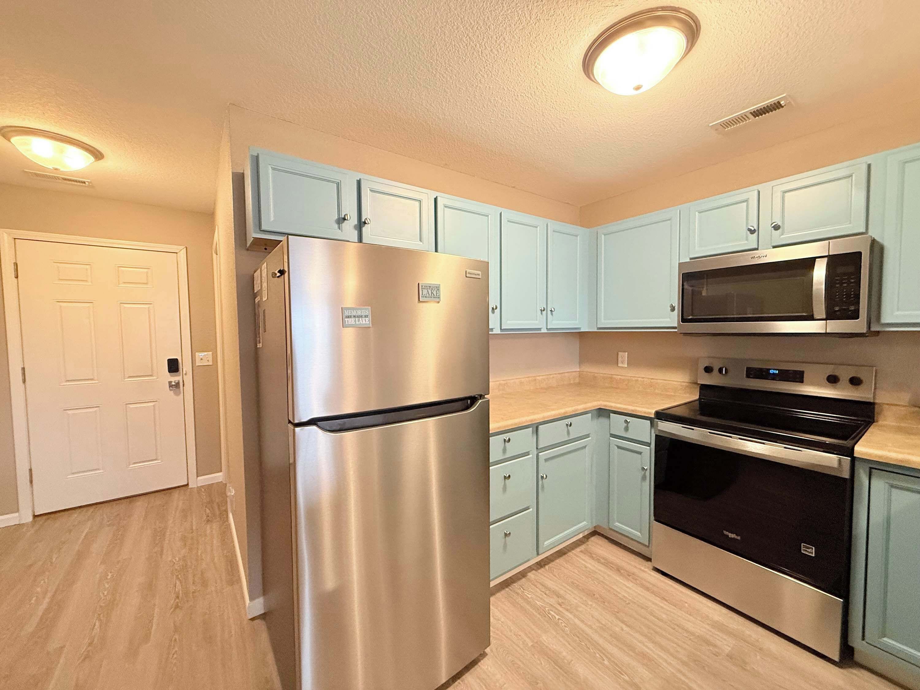 A kitchen with light blue cabinets, stainless steel appliances, and a white door.