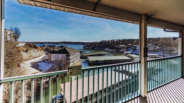 A balcony with a view of Lake Ozarks, a dock, and a sign indicating fishing activities. - Highland Lake View Incredible Location! (Lake Ozark)