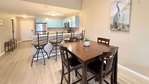 A dining area with a wooden table and chairs, a kitchen in the background, and a painting on the wall. - Highland Lake View Incredible Location! (Lake Ozark)