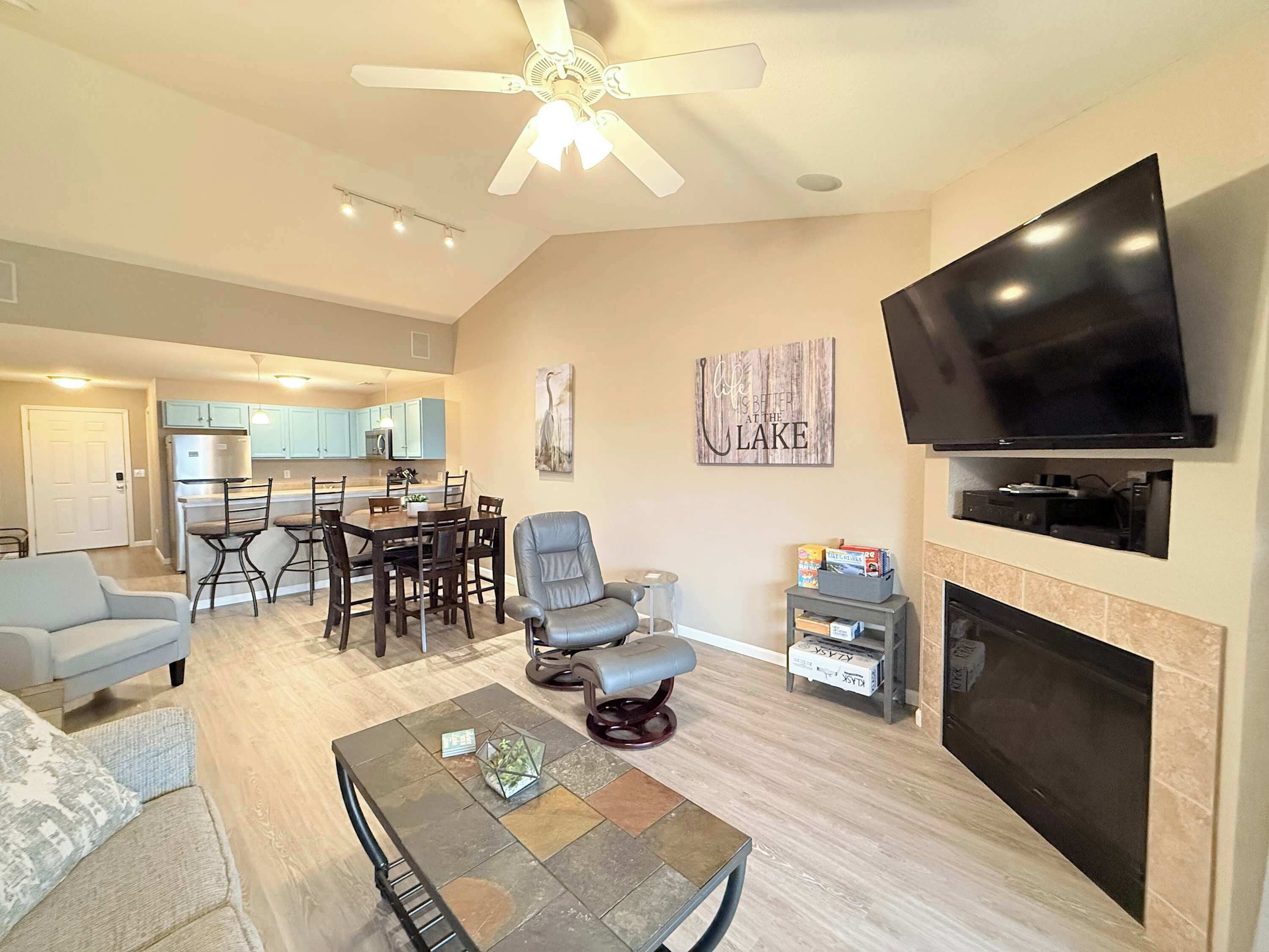 A living room with a flat-screen TV, a fireplace, a dining area, and a kitchen in the background.