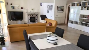 A living room with a yellow sofa, a TV, a fireplace, and a bookshelf. - Villa Tiziana, a wonderful oasis of peace and tranquility near Palermo (Monreale)