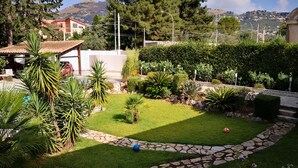 A well-maintained garden with a stone pathway, various plants, and a view of a hillside with buildings in the background. - Villa Tiziana, a wonderful oasis of peace and tranquility near Palermo (Monreale)