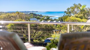 A balcony with a view of the ocean, trees, and a parked car.
