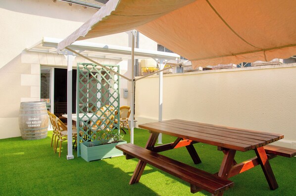 A patio area with a wooden picnic table, chairs, and a green lattice fence. - Le Relais du Jardin (Orbigny)