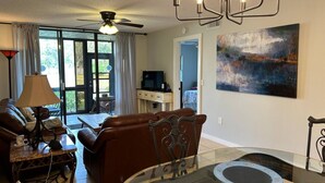 A living room with a brown leather sofa, a glass coffee table, a ceiling fan, and a painting on the wall.