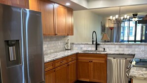 A modern kitchen with wooden cabinets, a stainless steel refrigerator, a dishwasher, and a granite countertop.