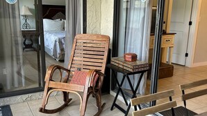 A wooden rocking chair and a bench on a tiled patio with a sliding glass door leading to a bedroom.