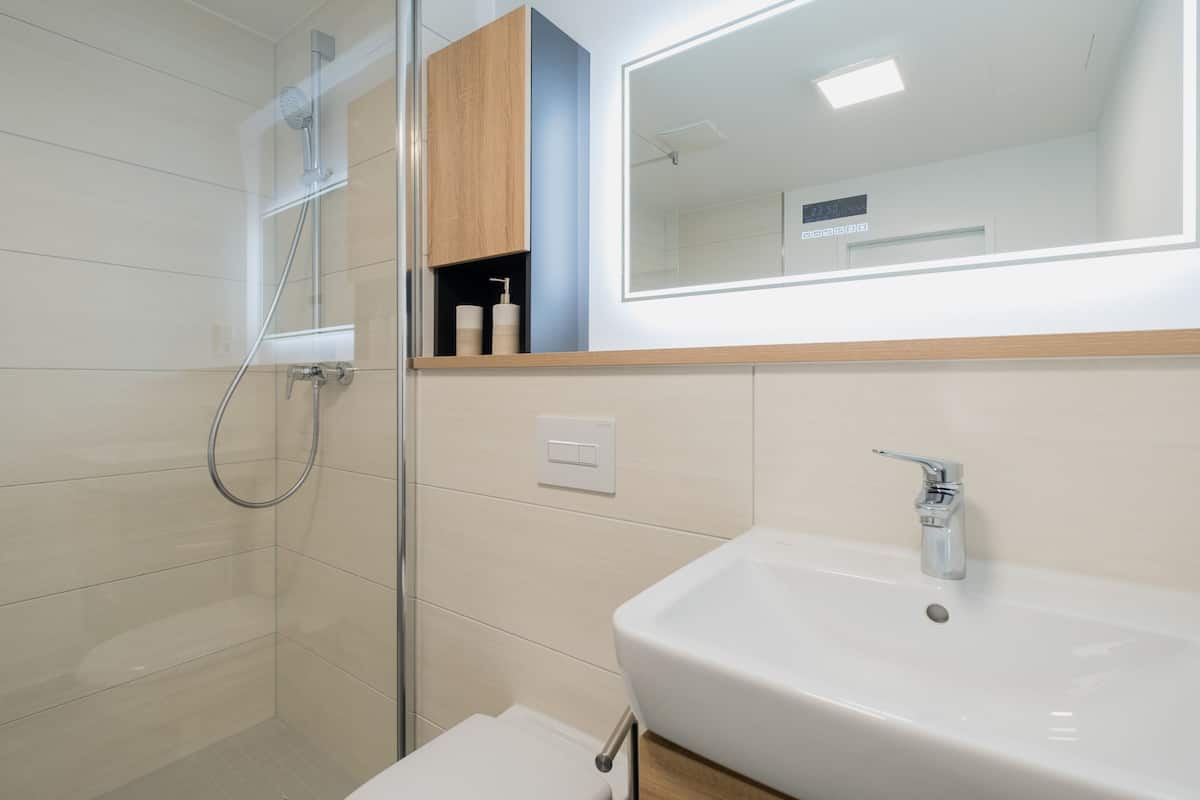 A modern bathroom with a glass-enclosed shower, a white sink, and a wooden vanity.