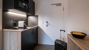 Une cuisine compacte équipée d’un four à micro-ondes, d’une machine à café et d’un saladier rempli de fruits posé sur le plan de travail.