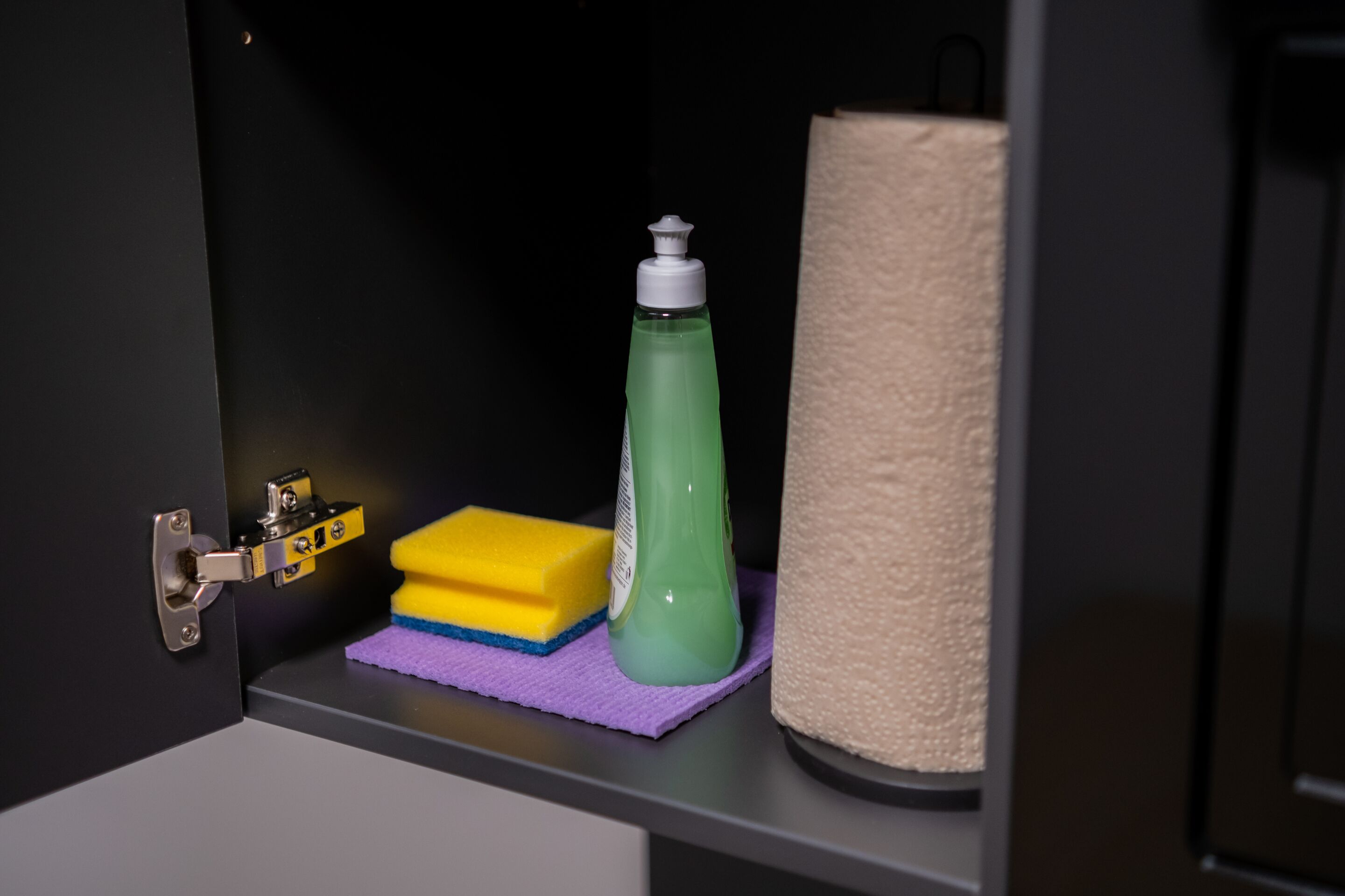 Un estante de baño con una botella de jabón líquido verde, una esponja amarilla y una toalla color beige.
