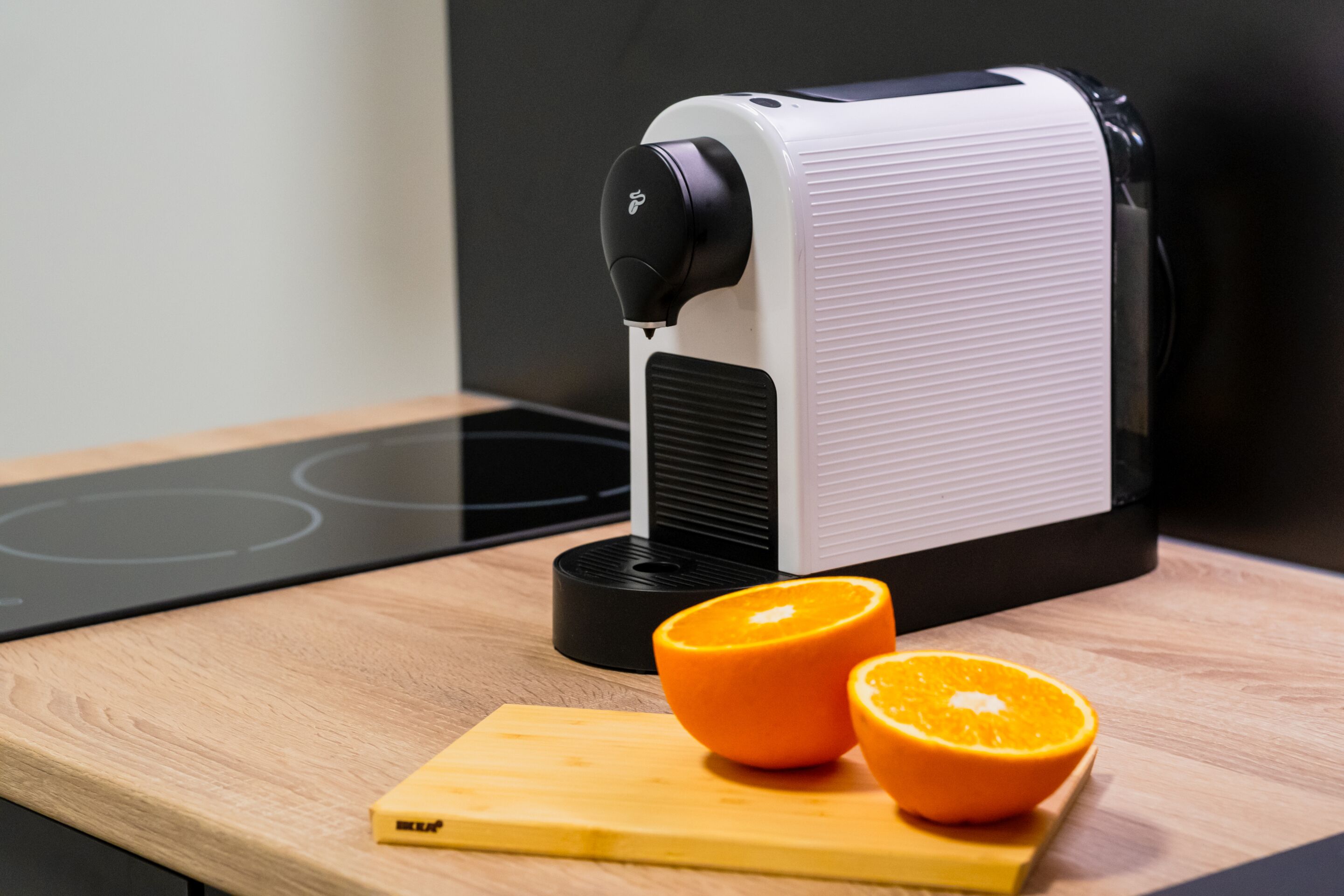 Een keuken met een moderne koffiemachine, een houten snijplank en twee partjes sinaasappel.