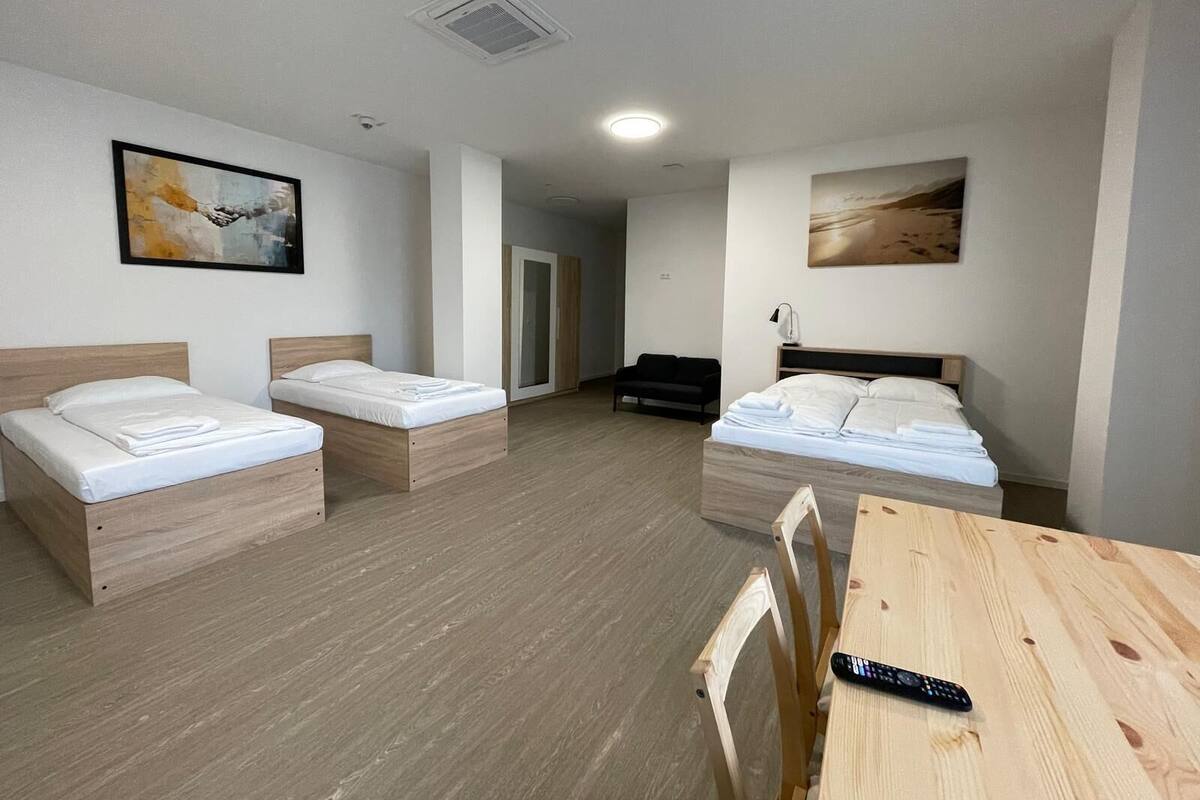 A hotel room with two single beds, a wooden table, a black sofa, and a remote control on the table.