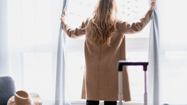 Une pièce avec une grande fenêtre, une chaise, une valise et un chapeau posé sur le sol.