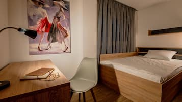 Quarto de hotel com cama de madeira, uma escrivaninha com um laptop, uma cadeira e um quadro na parede.