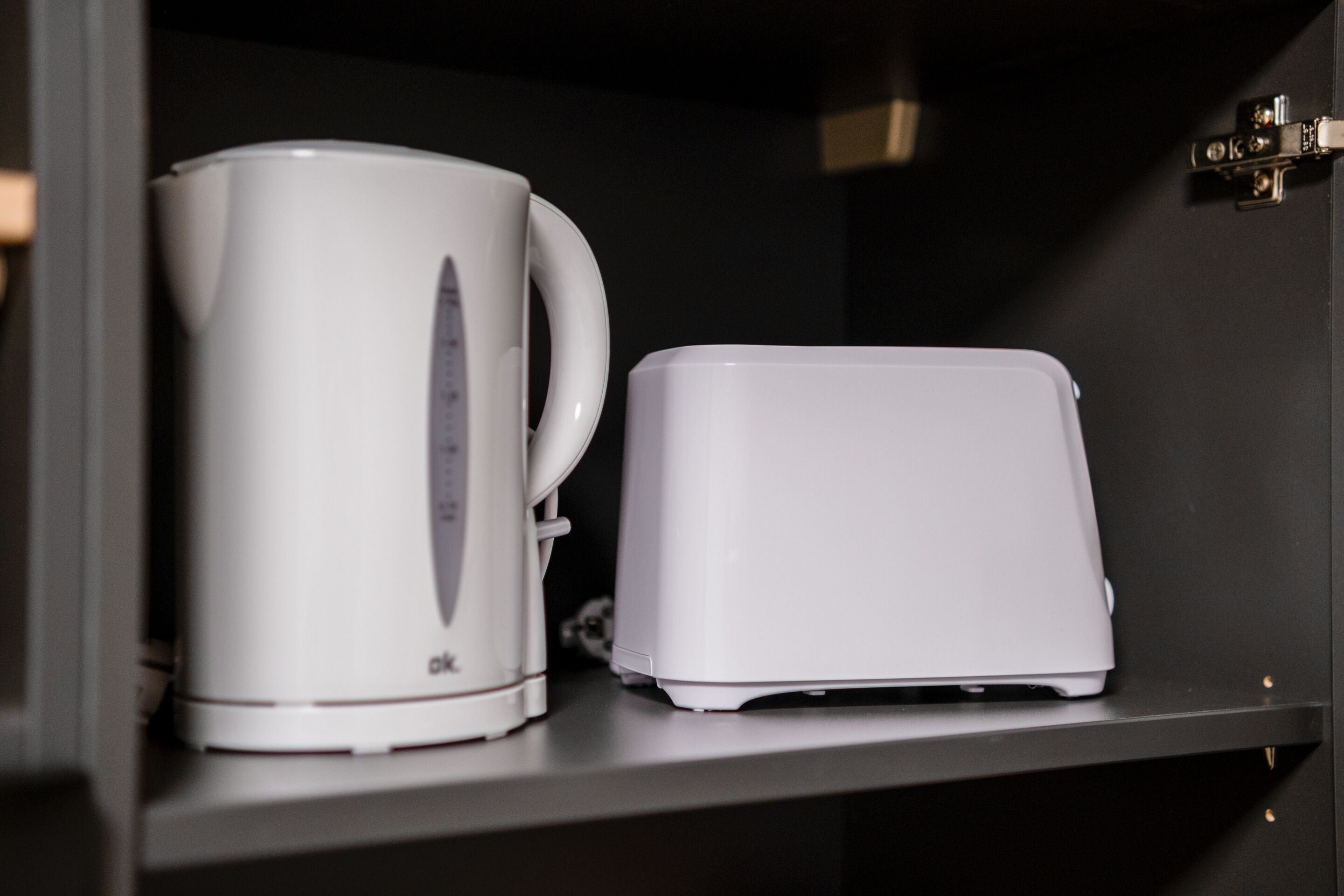 Eine weiße Kaffeemaschine und ein weißes Toaster stehen auf einem schwarzen Regal.