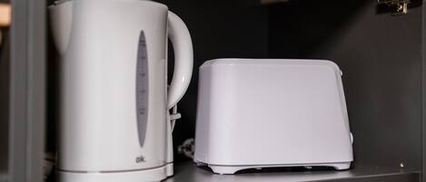 Eine weiße Kaffeemaschine und ein weißes Toaster stehen auf einem schwarzen Regal.