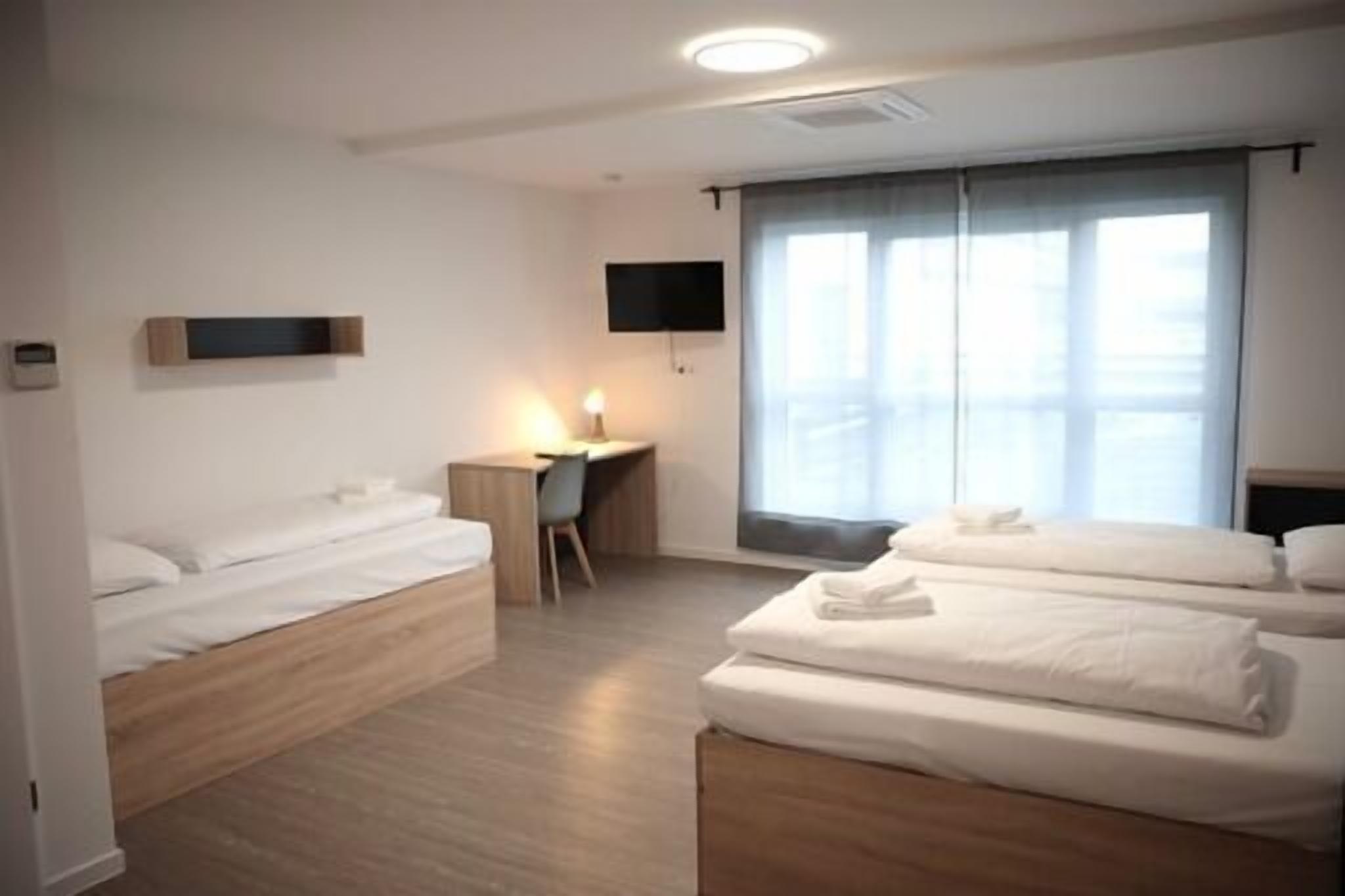 Habitación de hotel con dos camas, un escritorio, una silla, un televisor y un amplio ventanal con cortinas.