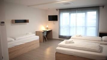 Habitación de hotel con dos camas, un escritorio, una silla, un televisor y un amplio ventanal con cortinas.