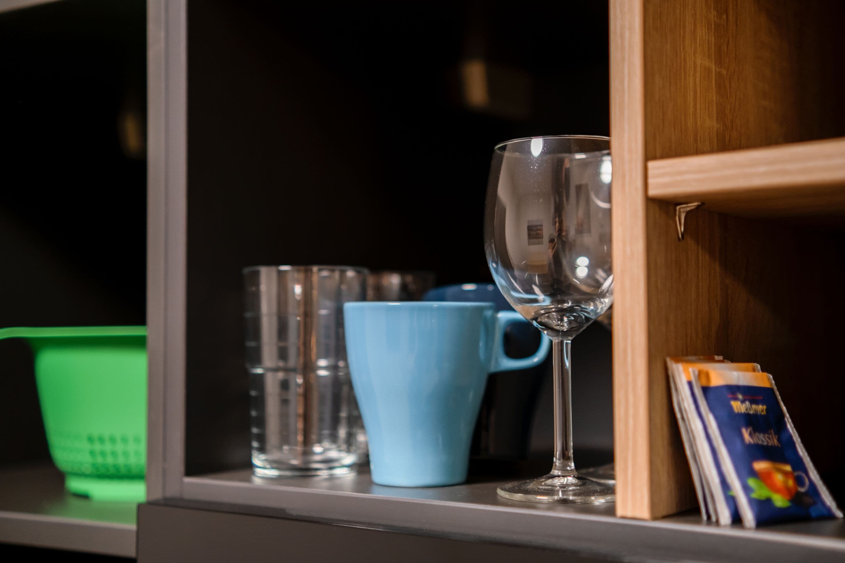 A shelf with a clear glass, a blue mug, and a green basket.