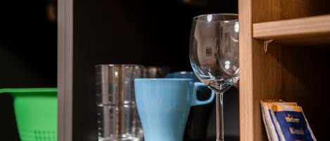 A shelf with a clear glass, a blue mug, and a green basket.