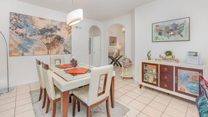 Un comedor con una mesa de vidrio, sillas blancas y un cuadro abstracto grande en la pared.