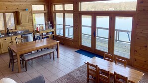 A wooden cabin with a kitchen, dining area, and large windows overlooking a lake.
