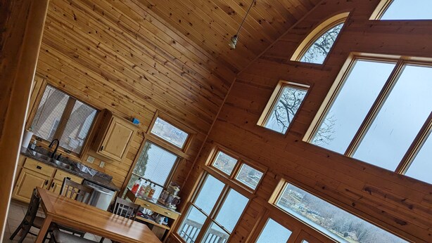 A spacious cabin with a dining area, kitchen, and large windows offering views of a lake.