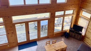A cabin with multiple large windows offering views of a lake and deck area with outdoor furniture.