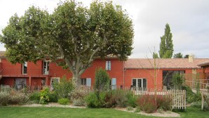 Un bâtiment rouge avec un toit en tuiles, entouré d’un jardin bien entretenu et doté d’une piscine.