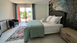 Une chambre à coucher comprenant un lit, une table de chevet, un bureau, une chaise, une grande fenêtre et un tableau accroché au mur.