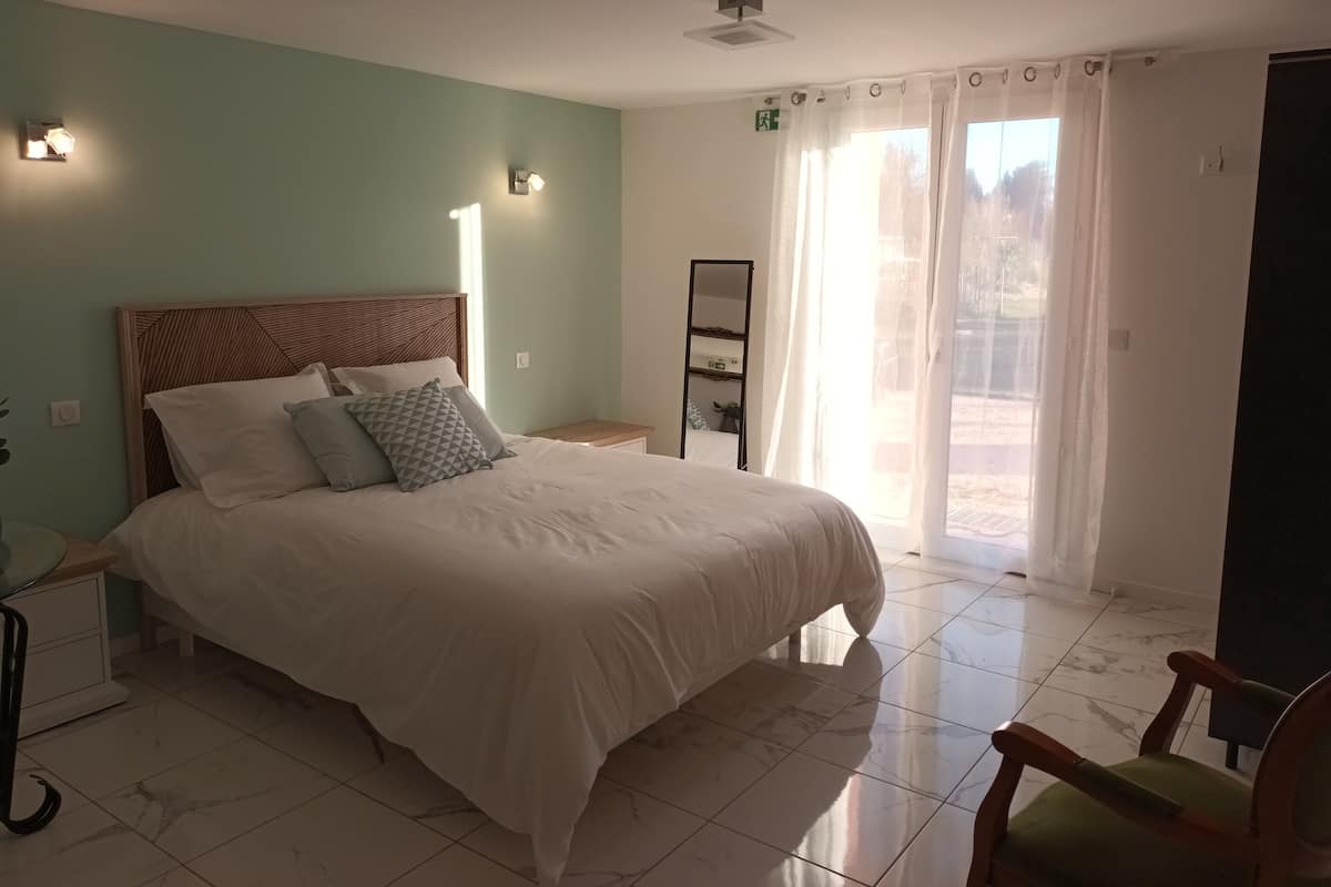Un dormitorio con cama, mesita de noche, una silla y una ventana con cortinas.