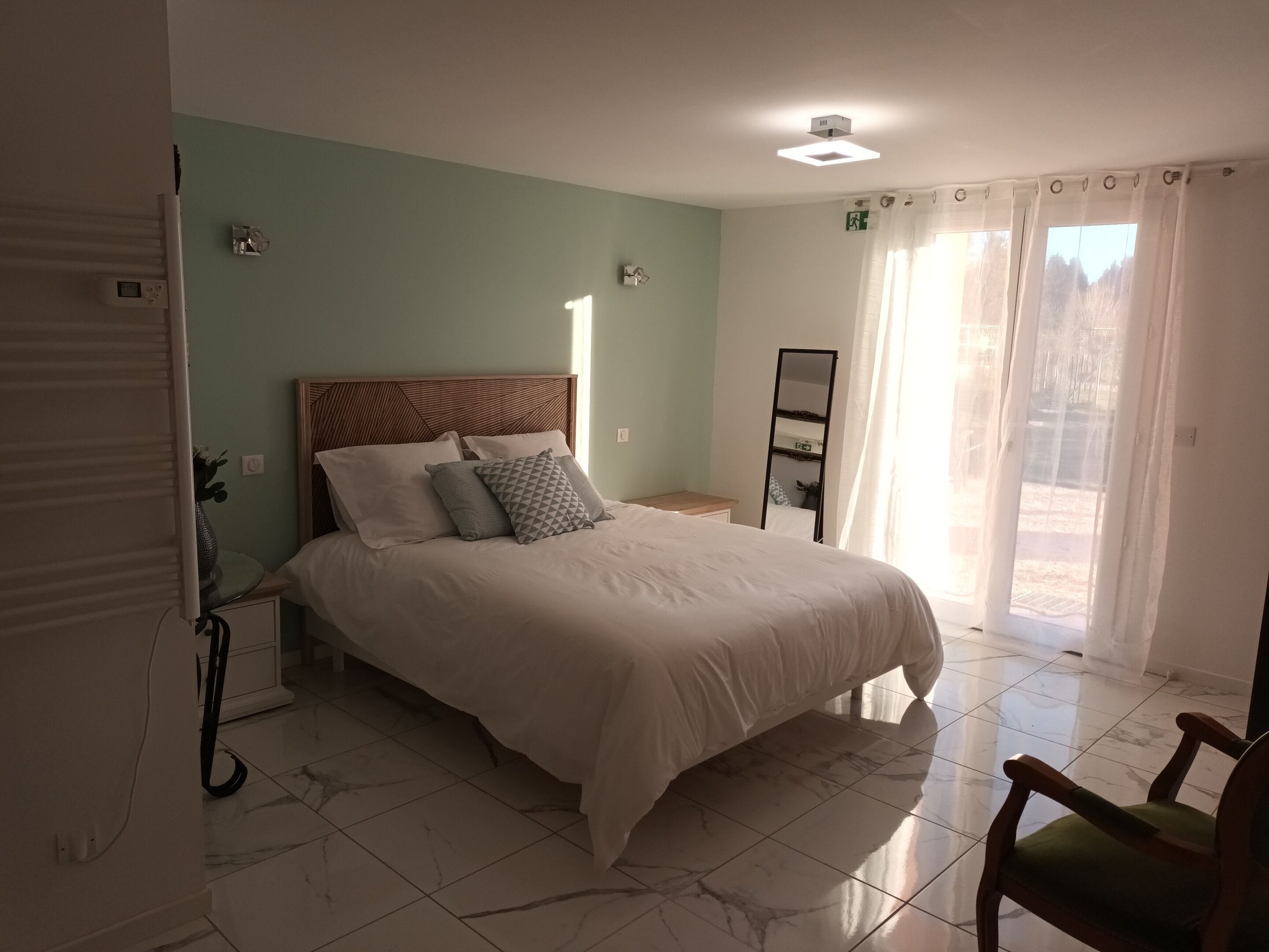 A bedroom with a large bed, a nightstand, a mirror, and a sliding glass door to a balcony.