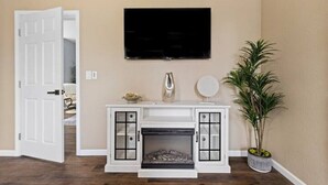 A room with a fireplace, a television mounted above it, and a potted plant.