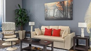 A living room with a beige sofa, red cushions, a coffee table, a painting of trees, a potted plant, and a chair with a cushion.