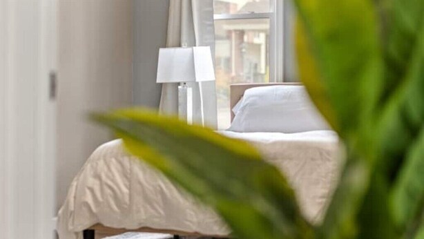 A bedroom with a bed, a nightstand, a lamp, and a window with curtains.