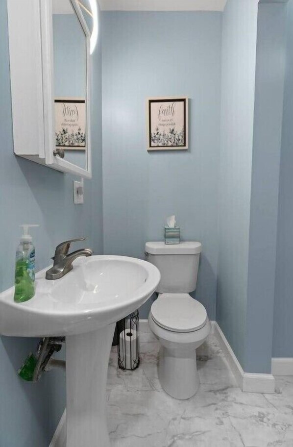 A bathroom with a white sink, a toilet, and two framed signs on the wall.