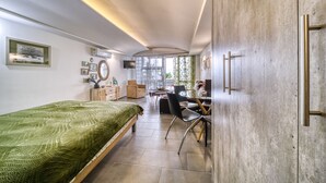 A modern bedroom with a bed, desk, and chair, a large window, and a view of the outdoors.