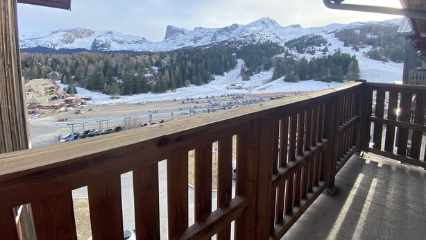 A wooden balcony with a view of a snowy mountain landscape, including a ski resort and forested areas. - Apartment at the foot of the slopes (Le Dévoluy)