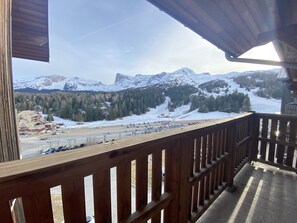 Ein Holzbalkon mit Blick auf eine verschneite Berglandschaft, darunter ein Skigebiet und bewaldete Flächen.