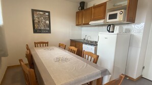 A small kitchen with a dining table, chairs, a refrigerator, a microwave, and wooden cabinets. - Apartment at the foot of the slopes (Le Dévoluy)