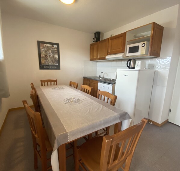 A small kitchen with a dining table, chairs, a refrigerator, a microwave, and wooden cabinets.