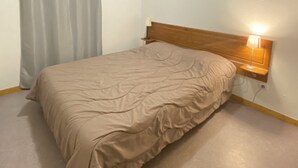 A bedroom with a bed, a nightstand with a lamp, a window with a curtain, and a plain wall. - Apartment at the foot of the slopes (Le Dévoluy)