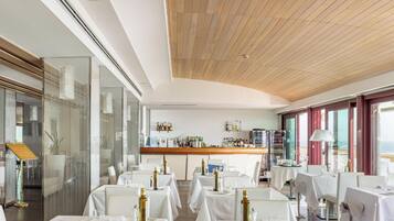 Un restaurante con zona de bar, mesas con mantelería blanca y vistas al mar a través de amplios ventanales.
