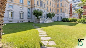 A courtyard with a stone pathway leading to a bridge, surrounded by a well-maintained lawn and buildings with classical architecture. - Hotiday Room Collection - Livorno Mascagni (Livorno)