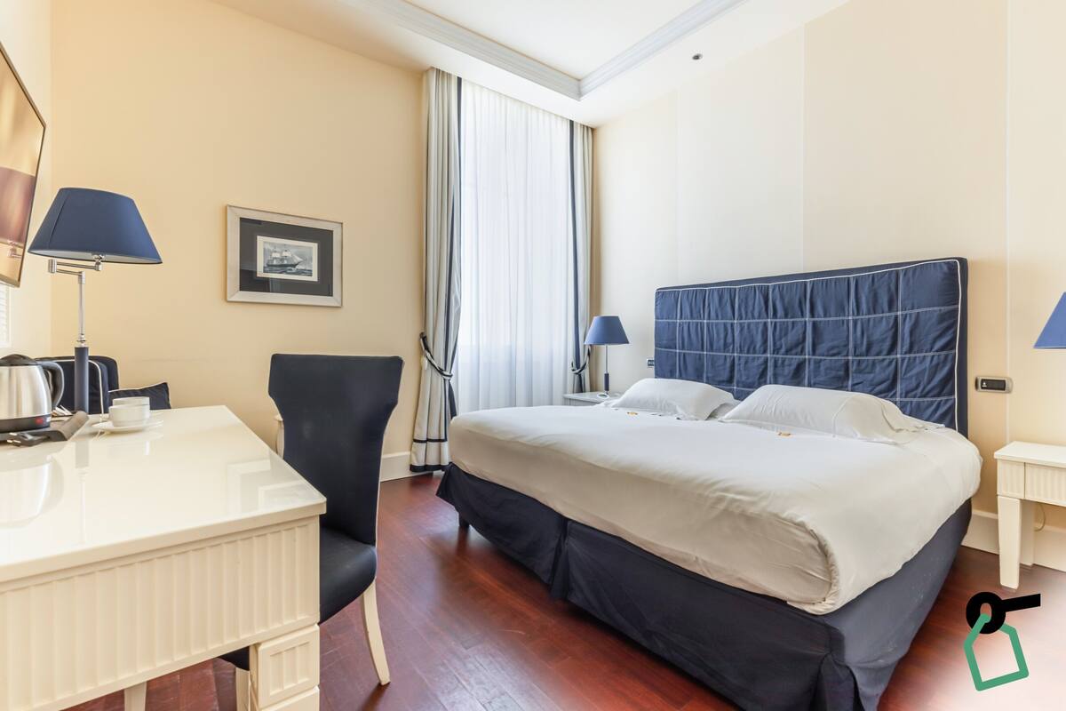Une chambre d’hôtel avec un lit, un bureau, une chaise, une lampe et un tableau au mur.