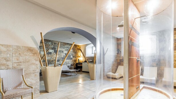 A modern bathroom with a glass-enclosed shower, a stone wall, and a seating area with wicker furniture. - Hotiday Room Collection - Livorno Mascagni (Livorno)