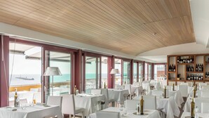 A restaurant with tables set for dining, large windows offering ocean views, and a wine rack on the wall. - Hotiday Room Collection - Livorno Mascagni (Livorno)