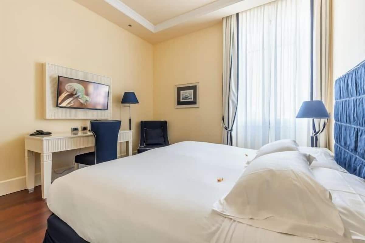 Une chambre d’hôtel avec un lit, un bureau, une chaise, une télévision et une fenêtre avec des rideaux.